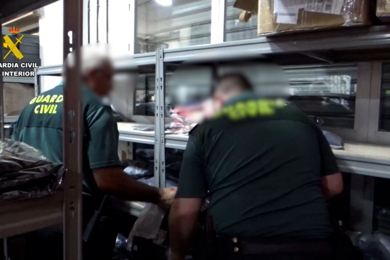 Dos guardias civiles realizan un registro en un almacén de efectos falsificados: perfumes, ropa, calzado...